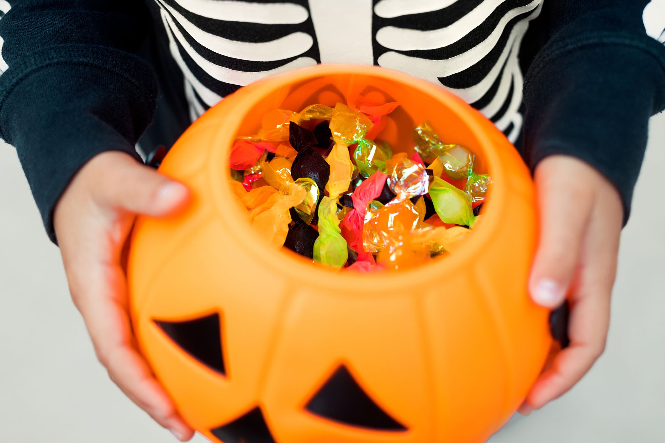 A child trick-or-treating with an orange jack-o-lantern candy bowl