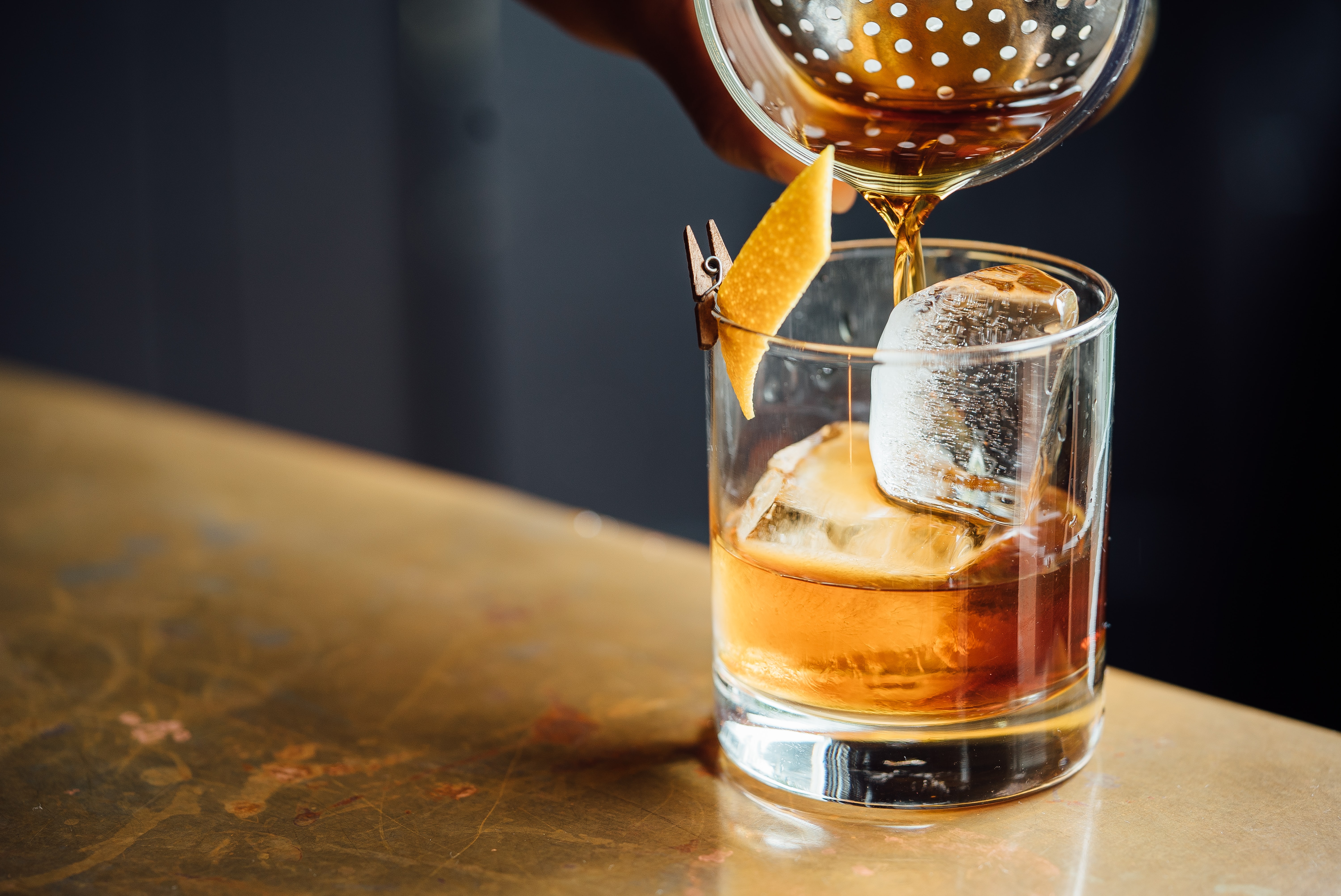 old fashioned cocktail being poured in a high ball glass